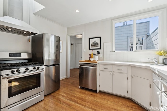 kitchen featuring light wood finished floors, tasteful backsplash, white cabinets, stainless steel appliances, and wall chimney range hood