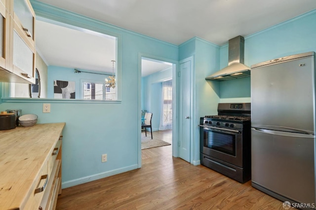 kitchen with appliances with stainless steel finishes, wood finished floors, crown molding, wall chimney range hood, and a chandelier