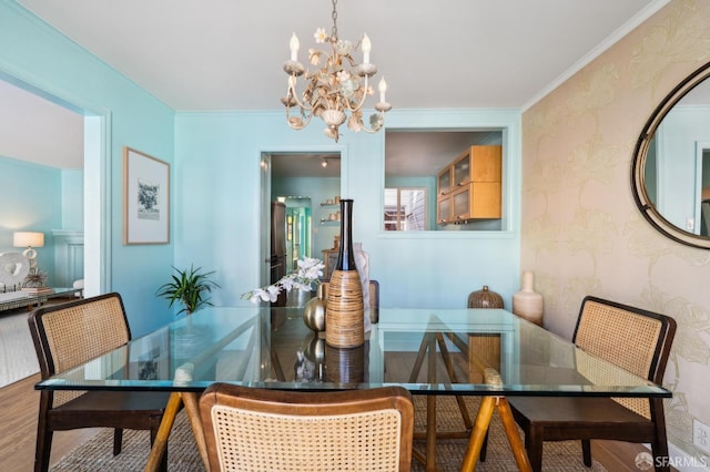 dining room with wallpapered walls, ornamental molding, wood finished floors, and an inviting chandelier