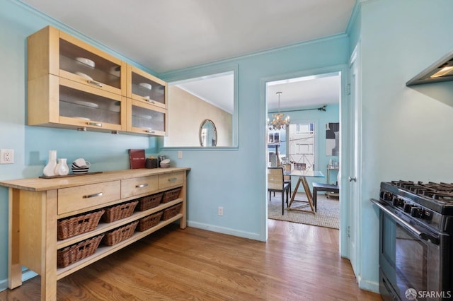 kitchen with wood finished floors, ornamental molding, gas stove, glass insert cabinets, and an inviting chandelier