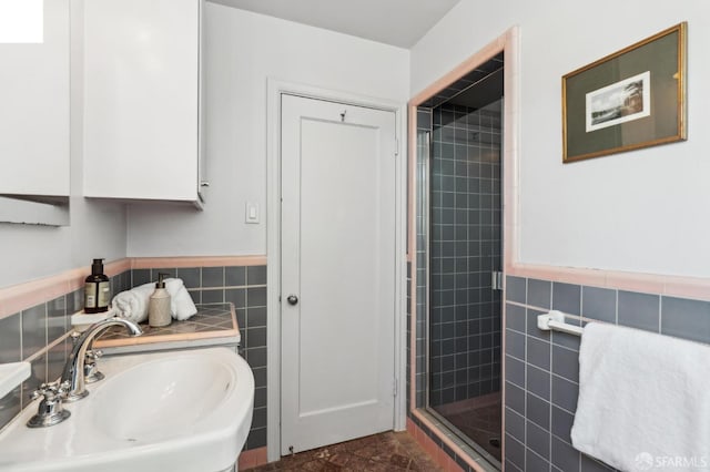 full bath with a wainscoted wall, a sink, tile walls, and a shower stall