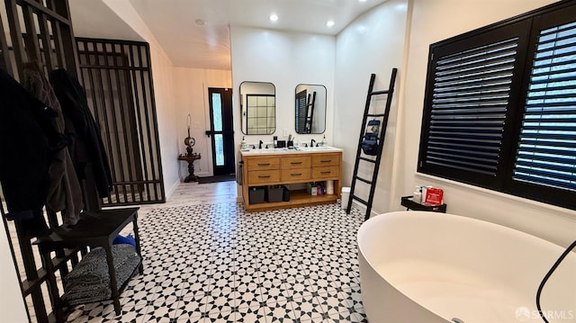 bathroom featuring baseboards, a freestanding bath, double vanity, and recessed lighting