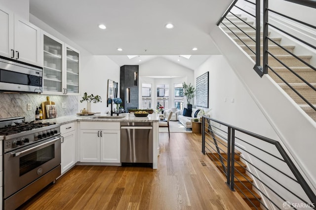 kitchen featuring white cabinets, appliances with stainless steel finishes, backsplash, and vaulted ceiling