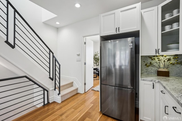 kitchen featuring stainless steel refrigerator, light stone countertops, light hardwood / wood-style flooring, decorative backsplash, and white cabinets