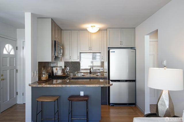 kitchen featuring sink, dark stone countertops, kitchen peninsula, stainless steel appliances, and backsplash