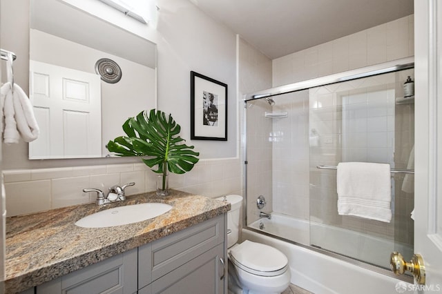 full bathroom with combined bath / shower with glass door, tile walls, vanity, tasteful backsplash, and toilet