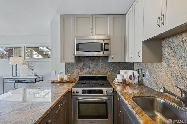 kitchen with sink, light stone counters, gray cabinets, stainless steel appliances, and decorative backsplash