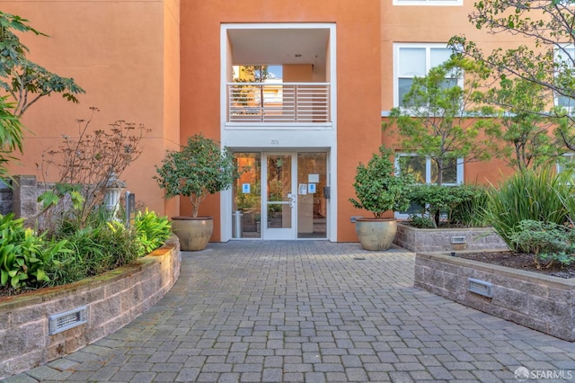 view of exterior entry with stucco siding, a balcony, visible vents, and a patio area