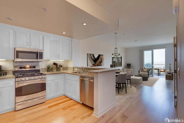 kitchen featuring open floor plan, appliances with stainless steel finishes, light wood-style floors, white cabinets, and a sink