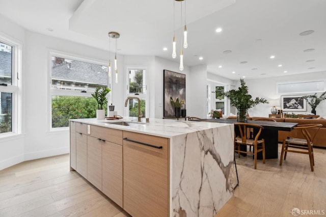 kitchen with a sink, light wood-type flooring, light stone counters, recessed lighting, and a kitchen island with sink