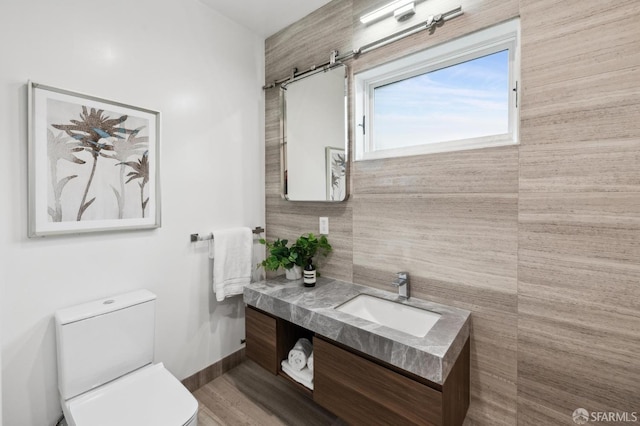 half bath featuring baseboards, toilet, wood finished floors, and vanity