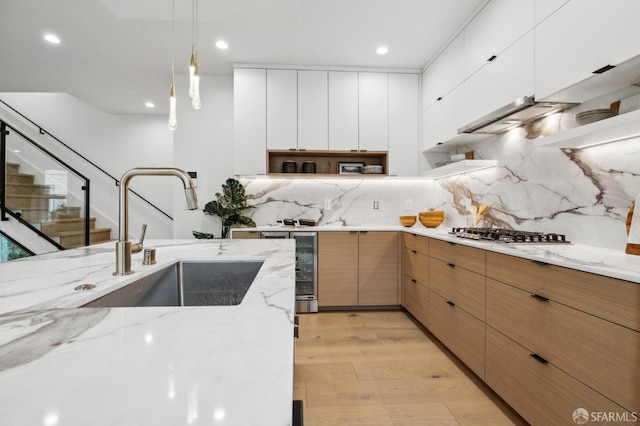 kitchen with backsplash, stainless steel gas cooktop, light wood-style floors, white cabinets, and a sink