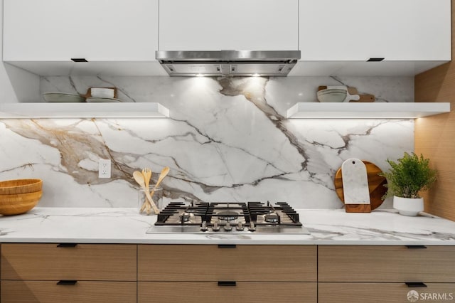 kitchen featuring modern cabinets, backsplash, ventilation hood, stainless steel gas stovetop, and light stone countertops