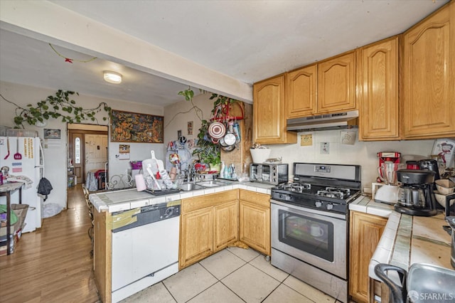 kitchen with white appliances, sink, light wood-type flooring, tile counters, and kitchen peninsula