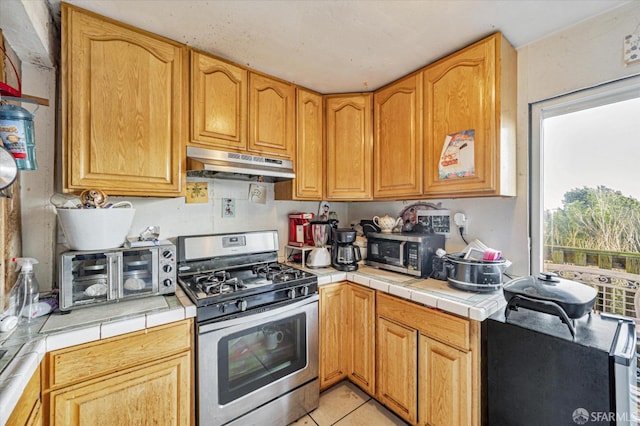 kitchen with appliances with stainless steel finishes, tile counters, and light tile patterned flooring