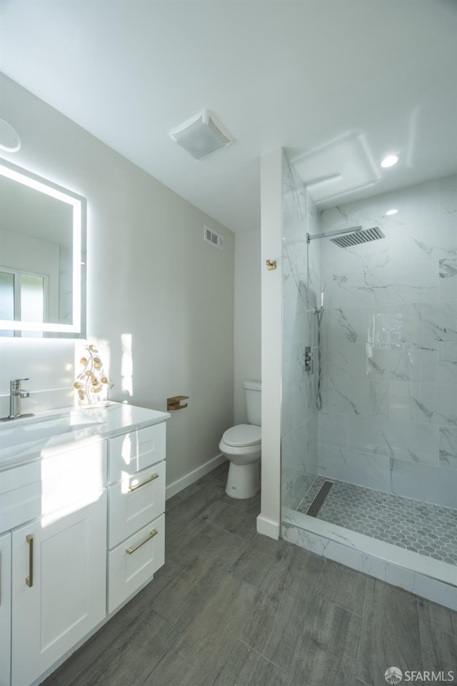 bathroom with toilet, a tile shower, and vanity