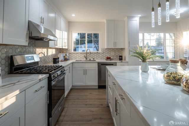 kitchen featuring stainless steel appliances, light stone counters, sink, white cabinetry, and decorative light fixtures