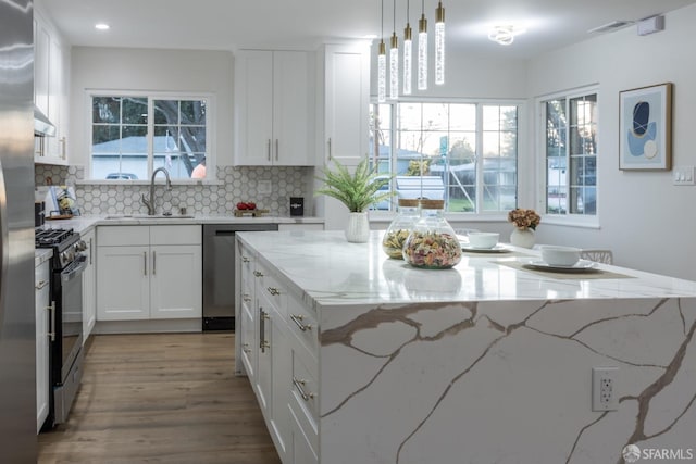 kitchen featuring stainless steel appliances, white cabinetry, light stone countertops, a kitchen island, and pendant lighting