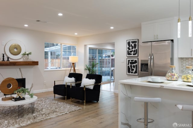 kitchen with white cabinets, light stone counters, tasteful backsplash, hanging light fixtures, and stainless steel fridge