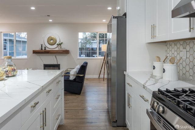 kitchen featuring light stone counters, wall chimney exhaust hood, tasteful backsplash, white cabinets, and appliances with stainless steel finishes