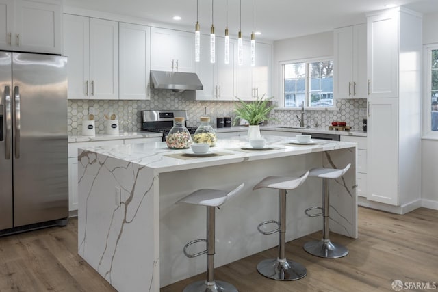 kitchen featuring light stone counters, decorative light fixtures, stainless steel appliances, a kitchen island, and white cabinetry