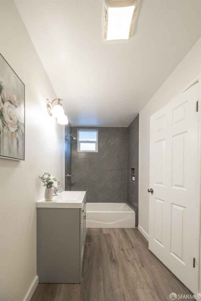 bathroom with hardwood / wood-style floors, tiled shower / bath combo, and vanity