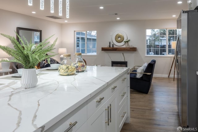 kitchen featuring stainless steel refrigerator, light stone countertops, plenty of natural light, hardwood / wood-style flooring, and white cabinetry