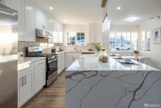 kitchen with light stone counters, decorative light fixtures, white cabinets, appliances with stainless steel finishes, and sink