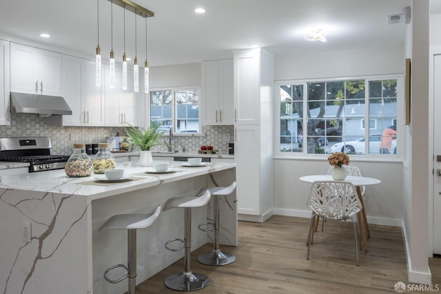 kitchen with a kitchen island, stainless steel range with gas cooktop, pendant lighting, and white cabinets