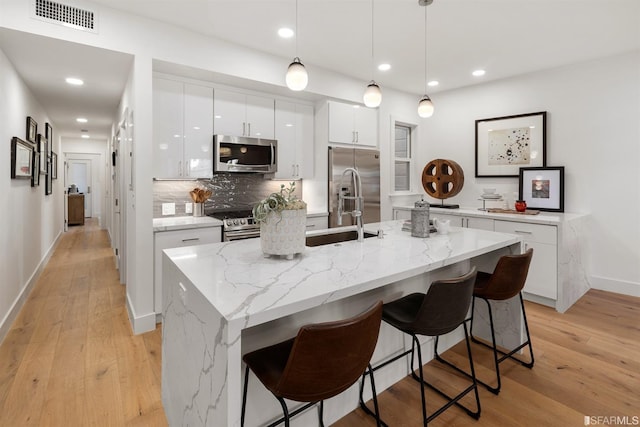 kitchen featuring visible vents, appliances with stainless steel finishes, a breakfast bar, white cabinetry, and backsplash