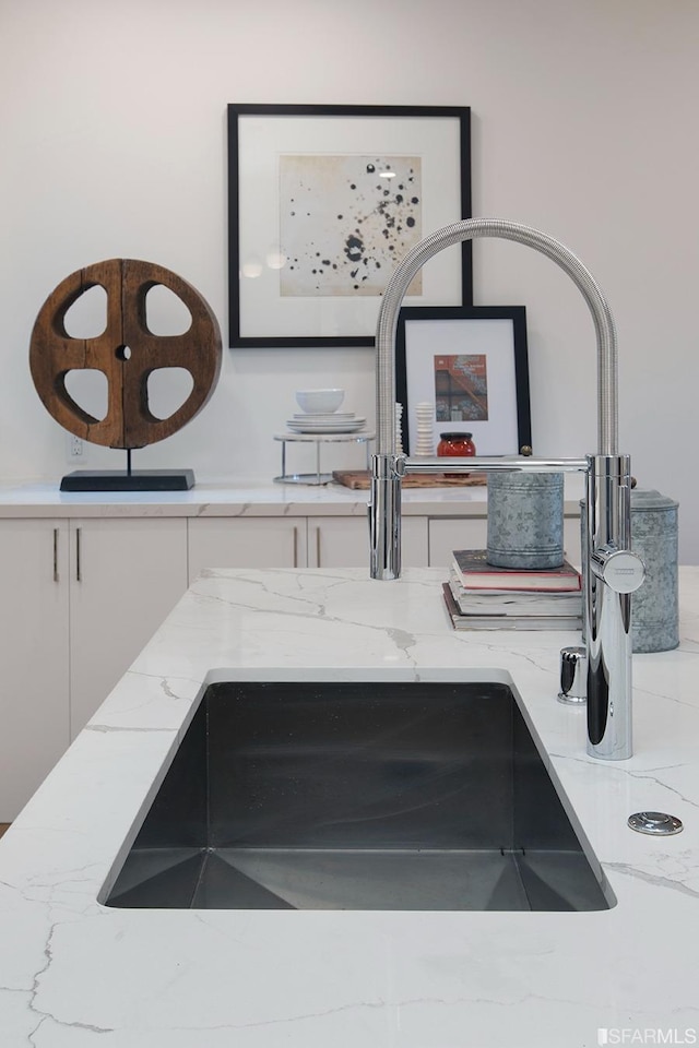 interior details featuring light stone counters, white cabinetry, and a sink