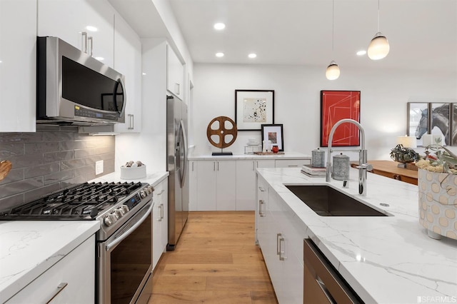 kitchen with light wood finished floors, white cabinets, appliances with stainless steel finishes, decorative light fixtures, and a sink