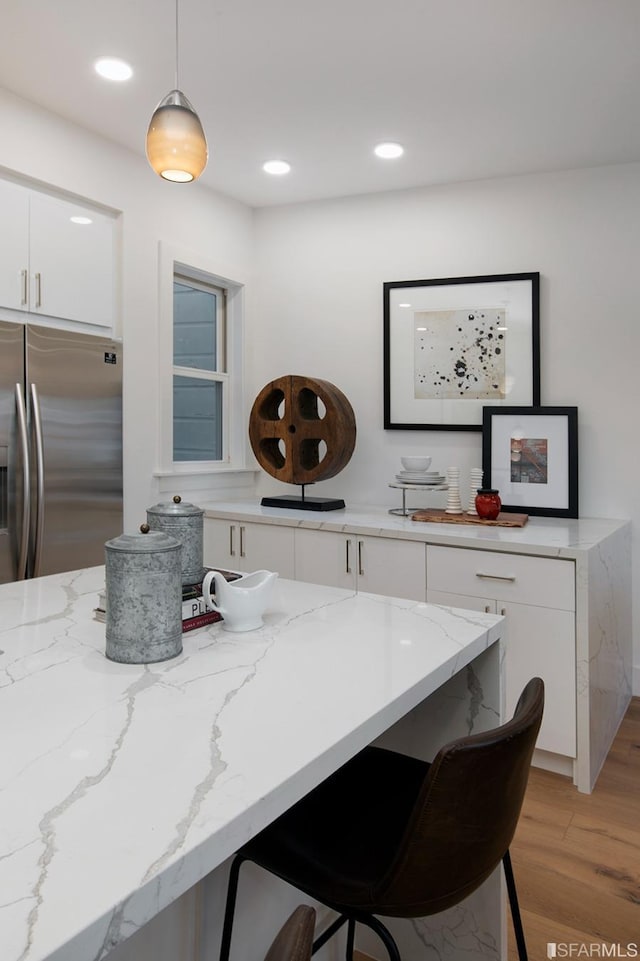 kitchen featuring light wood finished floors, stainless steel fridge with ice dispenser, decorative light fixtures, a kitchen bar, and white cabinetry