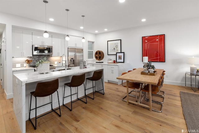 kitchen with stainless steel appliances, light wood finished floors, a breakfast bar area, and white cabinetry