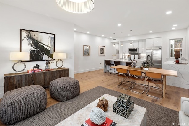 living area with baseboards, light wood-type flooring, and recessed lighting