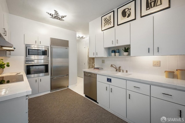 kitchen with white cabinetry, sink, light stone counters, backsplash, and built in appliances