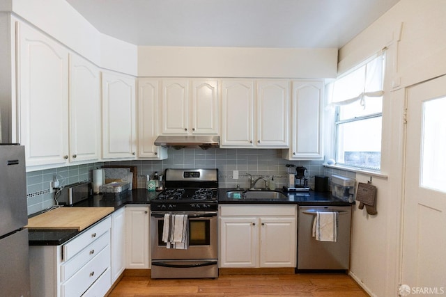 kitchen featuring decorative backsplash, appliances with stainless steel finishes, under cabinet range hood, white cabinetry, and a sink