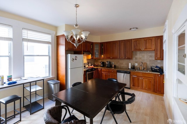 kitchen with a sink, appliances with stainless steel finishes, decorative backsplash, glass insert cabinets, and pendant lighting