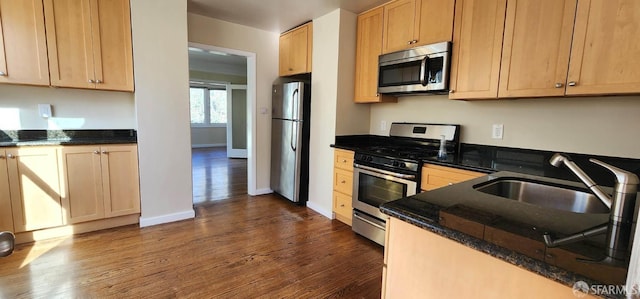 kitchen featuring dark stone counters, appliances with stainless steel finishes, dark wood-style flooring, a sink, and baseboards