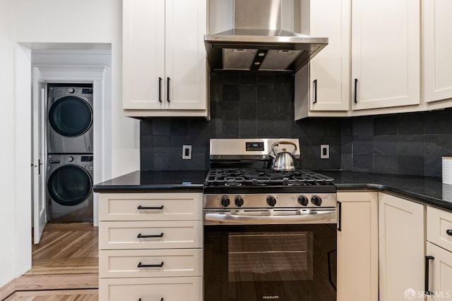 276 Funston Ave, San Francisco, CA 94118 - kitchen with stainless steel gas stove, stacked washer / drying machine, wall chimney exhaust hood, dark countertops, and light wood finished floors