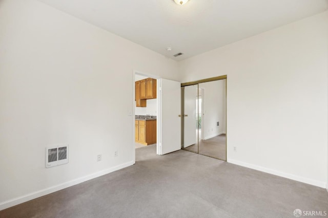 unfurnished bedroom featuring ensuite bath, light colored carpet, and a closet