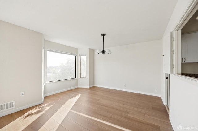 unfurnished room featuring a notable chandelier and light hardwood / wood-style flooring