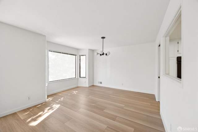 empty room featuring a notable chandelier and light wood-type flooring