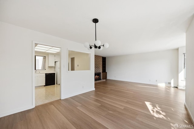 unfurnished living room featuring light hardwood / wood-style floors, a brick fireplace, and a notable chandelier