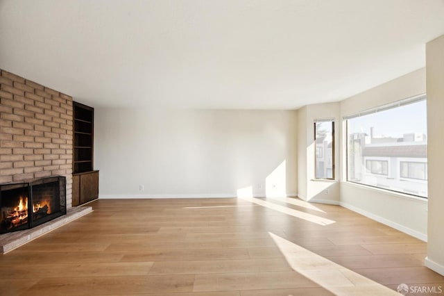 unfurnished living room with a brick fireplace and light hardwood / wood-style flooring