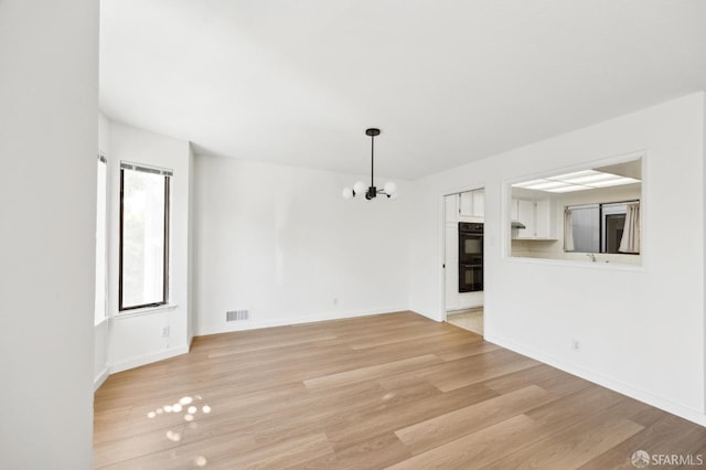 unfurnished living room featuring an inviting chandelier and light hardwood / wood-style flooring