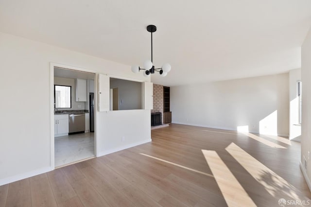 unfurnished living room featuring a brick fireplace, light hardwood / wood-style flooring, and a notable chandelier