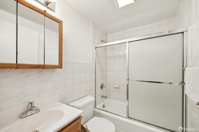 full bathroom featuring bath / shower combo with glass door, tile walls, vanity, and toilet