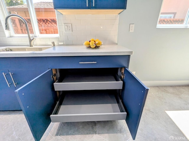interior details with a sink, blue cabinetry, baseboards, backsplash, and light countertops