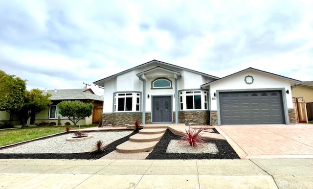 view of front of home with stucco siding, decorative driveway, an attached garage, and stone siding